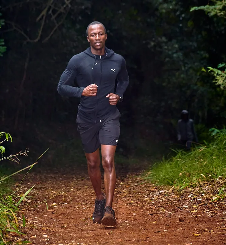 A runner in a black hoodie on a forest trail